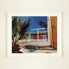Load image into Gallery viewer, White framed photograph by Richard Heeps. A colourful but derelict vintage motel sits in the blue Californian sun. Palm trees appear behind and to the side. 