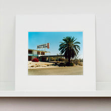 Load image into Gallery viewer, Mounted photograph by Richard Heeps. A derelict motel office sits on a dusty American road. A large palm tree sits at the front of the office&#39;s walkway.