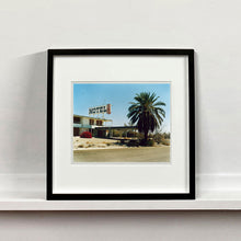 Load image into Gallery viewer, Black framed photograph by Richard Heeps. A derelict motel office sits on a dusty American road. A large palm tree sits at the front of the office&#39;s walkway.