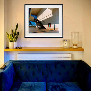 In situ photograph by Richard Heeps. The photograph has a metal staircase on the outside of a cream colour motel. The staircase has a ceiling but no sides so leads to blue sky. Behind the building is a blue sky and palm trees of the Californian Desert.