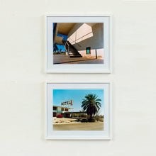 Load image into Gallery viewer, Two white framed photographs by Richard Heeps. The photograph has a metal staircase on the outside of a cream colour motel. The staircase has a ceiling but no sides so leads to blue sky. Behind the building is a blue sky and palm trees of the Californian Desert. The bottom photograph is of a run down motel sitting on a dusty road. At the end of the Motel walkway is a huge palm tree.