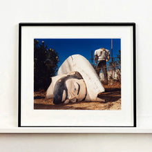 Load image into Gallery viewer, Black framed photograph by Richard Heeps. In the foreground of the photograph is a broken off head of a giant fibreglass sculpture of a cowboy (a Muffler Man). In the background set in a deep blue sky is the muffler man&#39;s headless torso.