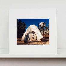 Load image into Gallery viewer, Mounted photograph by Richard Heeps. In the foreground of the photograph is a broken off head of a giant fibreglass sculpture of a cowboy (a Muffler Man). In the background set in a deep blue sky is the muffler man&#39;s headless torso.