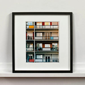 Black framed photograph by Richard Heeps. This is the balconies and balcony doors of 4 floors of flats located on the Rue Dezza. The colours of the walls alternate between red and grey but look different as the light catches them.