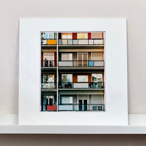 Mounted photograph by Richard Heeps. This is the balconies and balcony doors of 4 floors of flats located on the Rue Dezza. The colours of the walls alternate between red and grey but look different as the light catches them.