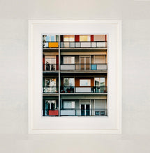 Load image into Gallery viewer, White framed photograph by Richard Heeps. This is the balconies and balcony doors of 4 floors of flats located on the Rue Dezza. The colours of the walls alternate between red and grey but look different as the light catches them.