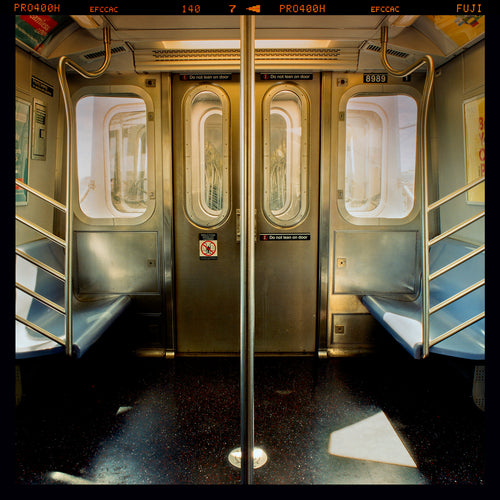 Photograph by Richard Heeps. Photograph of the inside of a subway car, looking towards the coaches through the emergency adjoining door. A grab pole sits in the middle.