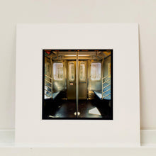 Load image into Gallery viewer, Mounted photograph by Richard Heeps. Photograph of the inside of a subway car, looking towards the coaches through the emergency adjoining door. A grab pole sits in the middle.