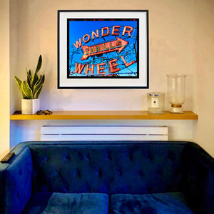 Framed artwork of 'Wonder Wheel' on a wall above a blue sofa artwork by Richard Heeps