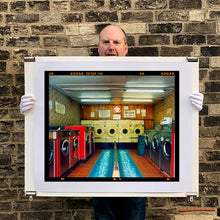 Load image into Gallery viewer, A photograph held by photographer Richard Heeps. A laundrette with washing machines on each wall and a double sided seat in the middle.