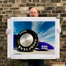 Load image into Gallery viewer, Photograph held by photographer Richard Heeps. This photograph has the tyre and the very front tip of a drag car. The car&#39;s name is written on the front end &quot;God Speed&quot;. Behind the car are white vertical clouds shooting through a blue sky.