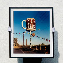 Load image into Gallery viewer, Photograph held by photographer Richard Heeps. A giant model of a mug with Bob&#39;s Root Beer written on it sits on top of a giant pole. There is bunting hanging from the pole. It sits alongside a power line on a remote looking American country road.