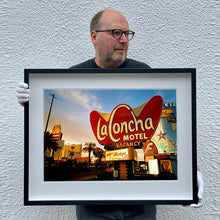 Load image into Gallery viewer, Black framed photograph held by Richard Heeps. This photograph is of the outside of La Concha Motel. The gold flamboyant La Concha lettering is set on a big red background. Below the motel sign is NO VACANCY with just VACANCY lit in red, below this sits a sign for Budget rent a car. Other signs and palm trees are the background together with a blue sky.