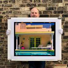 Load image into Gallery viewer, Photograph held by photographer Richard Heeps. Palm Springs Pool Side II showcases classic mid-century Palm Springs California architecture. Cool blue skies and pool with accents of pink and almost neon yellow. 