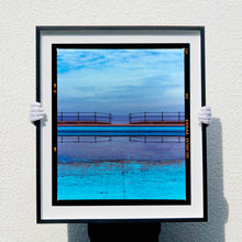 Load image into Gallery viewer, Photograph by Richard Heeps. The blue bay at Llandudno, cut across the middle with path and railings with a gap right in the middle.