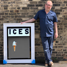 Load image into Gallery viewer, Photograph by Richard Heeps.  Richard Heeps holds a white framed print. At the top of the print, black letters spell out ICES and below is depicted a 99 icecream cone sitting left of centre against a grey coloured background.  