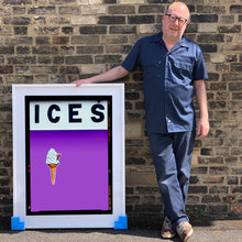 Load image into Gallery viewer, Photograph by Richard Heeps.  Richard Heeps holds a white framed print. At the top of the print, black letters spell out ICES and below is depicted a 99 icecream cone sitting left of centre against a lilac coloured background.  
