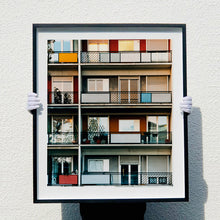 Load image into Gallery viewer, Photograph held by photographer Richard Heeps. This is the balconies and balcony doors of 4 floors of flats located on the Rue Dezza. The colours of the walls alternate between red and grey but look different as the light catches them.
