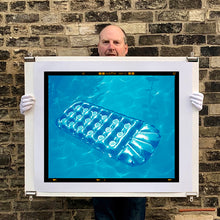 Load image into Gallery viewer, Photograph held by photographer Richard Heeps. A transparent blue lilo is sun bathing on a blue pool. 
