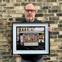 Load image into Gallery viewer, News Stand Milan, Italian street photography by Richard Heeps holding a small print framed in black.