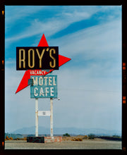 Load image into Gallery viewer, Photograph by Richard Heeps edged by film rebate. A roadside sign on Route 66 in America. The word ROY&#39;S appears in a black sign with a bit red arrow pointing to the left ground, below this VACANCY and on a green square the words MOTEL and CAFE.