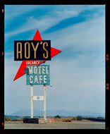 Photograph by Richard Heeps edged by film rebate. A roadside sign on Route 66 in America. The word ROY'S appears in a black sign with a bit red arrow pointing to the left ground, below this VACANCY and on a green square the words MOTEL and CAFE.