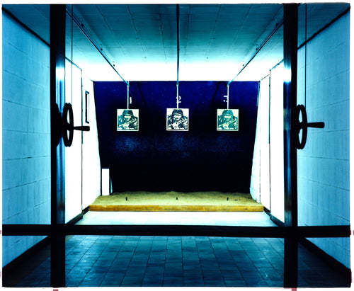 Photograph by Richard Heeps. A shooting range with 3 targets depicting soldiers. The back drop is blue surrounded by neon giving the whole range a blue glow.