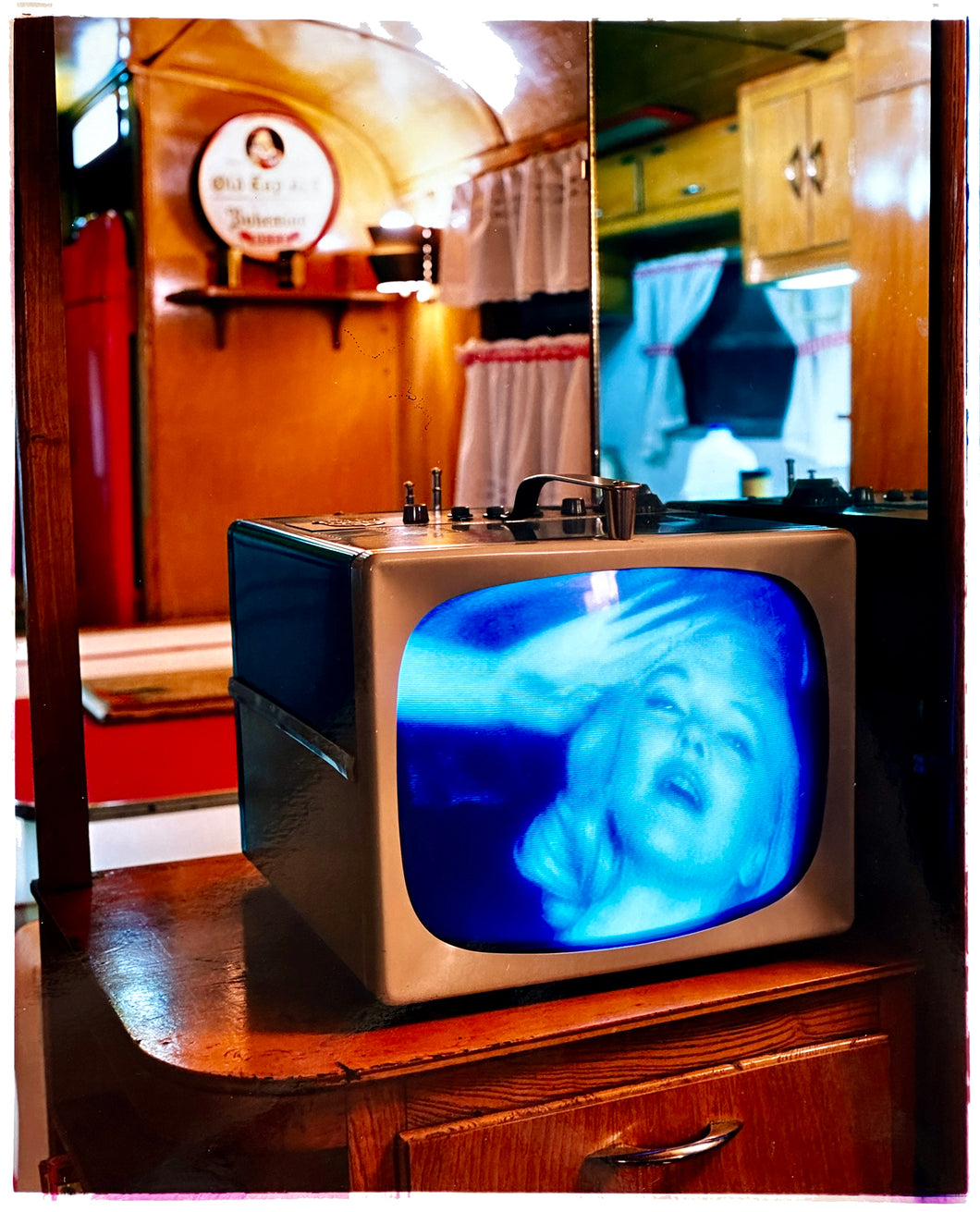 Photograph by Richard Heeps. A retro small brown television sits on a wooden table displaying a black and white film, with the face of Marilyn Monroe filling the screen, it shows as blue and white. In the background of the television is a warm wood-panelled light.