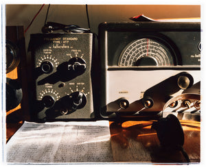 Photograph by Richard Heeps. Station X sits on a desk in front of it is a handwritten sheet of numbers and the headphones sit on the right hand side.