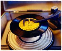 Load image into Gallery viewer, Photograph by Richard Heeps. A black vinyl with a yellow label sits high on the spindle of a deck under the overarm.