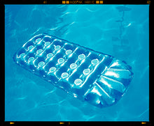 Load image into Gallery viewer, Photograph by Richard Heeps. A transparent blue lilo is sun bathing on a blue pool. 