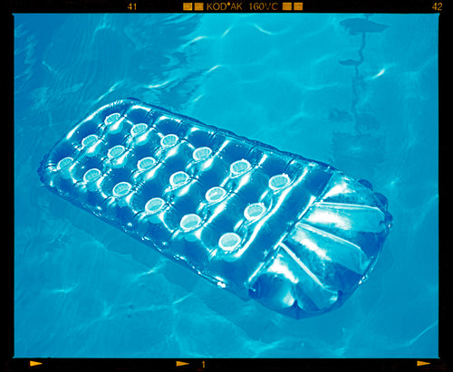 Photograph by Richard Heeps. A transparent blue lilo is sun bathing on a blue pool. 