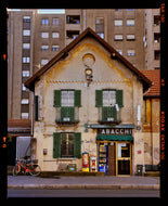Photograph by Richard Heeps. A traditional Italian Tobacconist shop, here in a Swiss Cottage style building set against a vast urban apartment block.