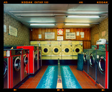 Load image into Gallery viewer, Photograph by Richard Heeps. A laundrette with washing machines on each wall and a double sided seat in the middle. 