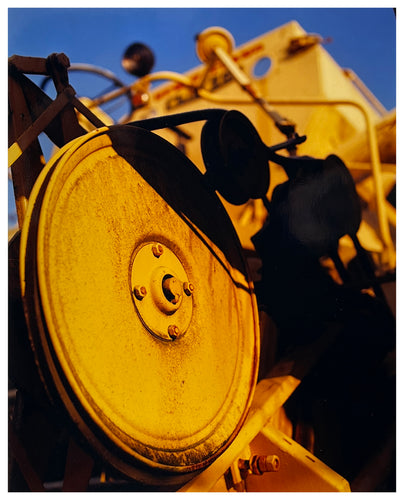 Photograph of Richard Heeps.  A yellow combine harvester is bathed in golden light with a blue sky behind.