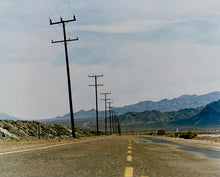 Load image into Gallery viewer, An open road in Amboy, California, featuring telephone poles disappearing into the mountainous distance. This classic and timeless landscape photograph is part of Richard Heeps&#39; &#39;Dream in Colour&#39; series. 