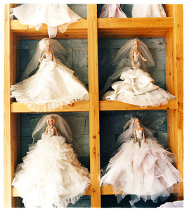 Four Barbie dolls in wedding dressed on a shelf.