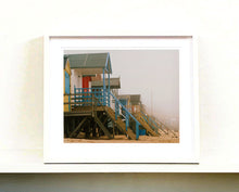 Load image into Gallery viewer, &#39;Beach Huts&#39;, photographed by Richard Heeps in one of his favourite areas of the UK, the port town of Wells-next-the-sea, Norfolk. This piece captures the classic quintessential beach hut on an atmospherically foggy day.