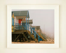 Load image into Gallery viewer, &#39;Beach Huts&#39;, photographed by Richard Heeps in one of his favourite areas of the UK, the port town of Wells-next-the-sea, Norfolk. This piece captures the classic quintessential beach hut on an atmospherically foggy day.