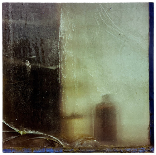 Photograph by Richard Heeps. The silhouette of a bottle behind a cracked, frosted window pane. 