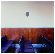 Load image into Gallery viewer, Photograph by Richard Heeps. Rows of empty blue seats facing side ways on, a Fisherman&#39;s Mission badge hangs on the white wall.