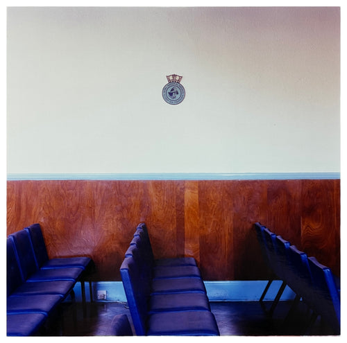 Photograph by Richard Heeps. Rows of empty blue seats facing side ways on, a Fisherman's Mission badge hangs on the white wall.