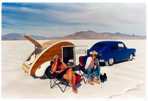 'Christine's '52 Henry J & teardrop' was captured in Bonneville Salt Flats, Utah, the iconic home of speed. This photograph shows the mountains in the distance meeting and contrasting with the flatness of the salt pan, whilst a pair of retro spectators look out at the speeding cars in the distance.