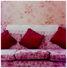 Load image into Gallery viewer, Photograph by Richard Heeps. A purple flowered sofa sits with three red cushions neatly placed and a crocheted antimacassar.  The background is a contrasting peach flowered wallpaper. 