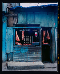 Photograph by Richard Heeps. A butcher's window in the North of India.  A blue painted shack with meat hanging in the window and door.
