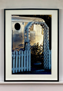 Part of Richard Heeps' 'Dream in Colour' series, this photograph features a white picket fence entrance to the Royal Mansion at the Shady Dell Trailer Park in Bisbee. Arizona. 