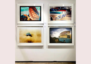 A moody Fenland sky is backdrop to a classic British Fish & Chips Van. The typography and the van itself has a fun fairground feel, contrary to the muted tones of this piece. Part of Richard Heeps series, 'A View of the Fens from the Car with Wings'.