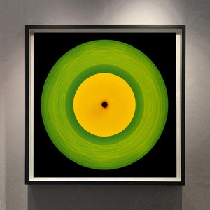 Photograph by Richard Heeps.  A green vinyl record with circular grooves is central with an orange centre sitting on a black background.