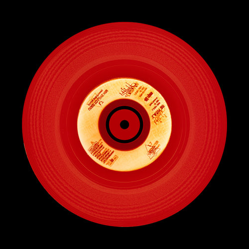 Photograph of a red vinyl record on a black background.  Photographers Heidler and Heeps