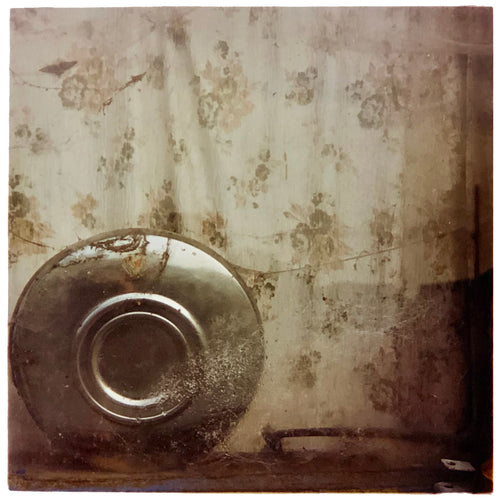Photograph by Richard Heeps. A hub cap sits in the corner, behind it is a faded brown patterned curtain. 